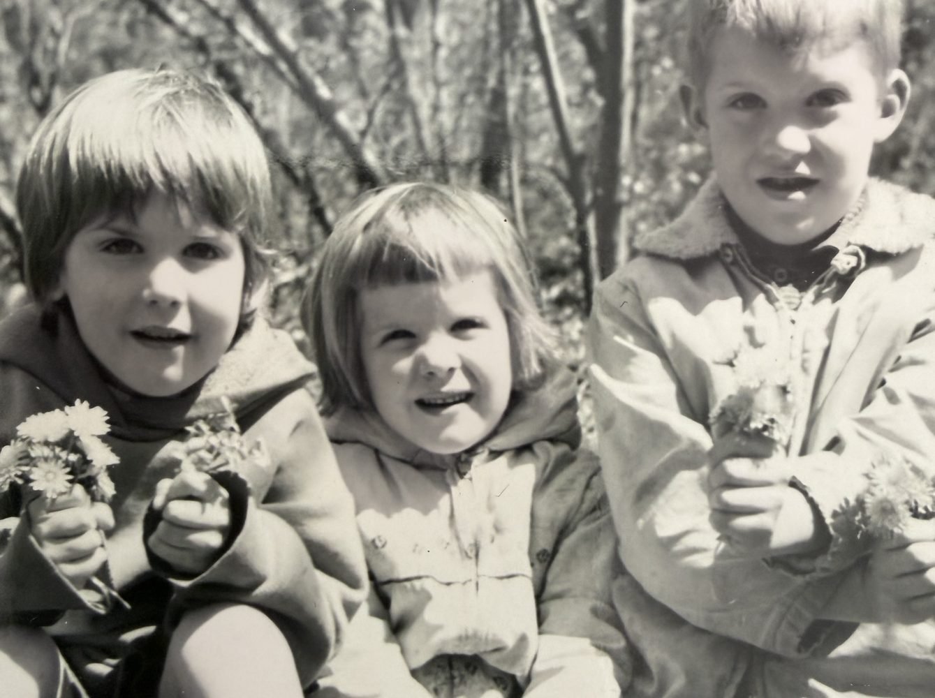 Jonathan with his sisters as young children, holding daisies